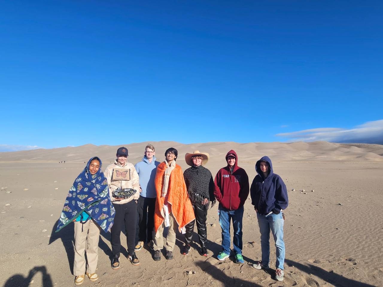 The IEEE and COSGC team standing together in the sand dunes under a clear blue sky